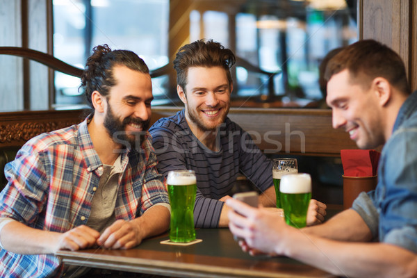friends with smartphone drinking green beer at pub Stock photo © dolgachov