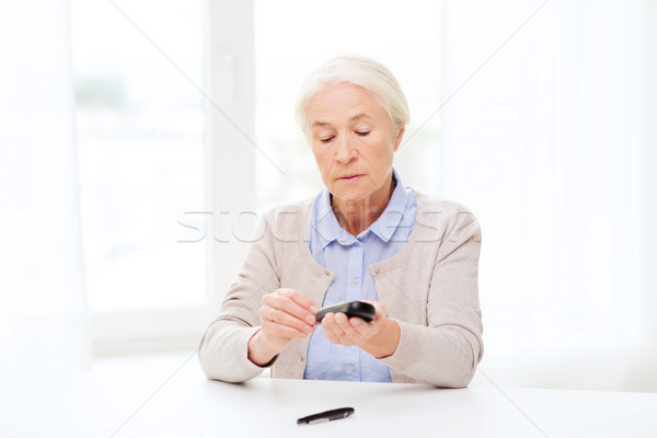 senior woman with glucometer checking blood sugar Stock photo © dolgachov