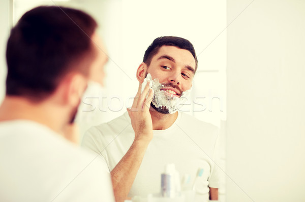 happy man applying shaving foam at bathroom mirror Stock photo © dolgachov