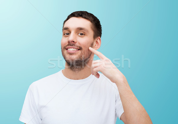 Uśmiechnięty młodych przystojny mężczyzna wskazując policzek zdrowia Zdjęcia stock © dolgachov