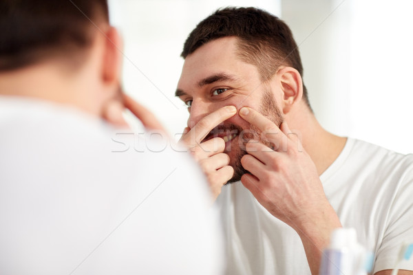 smiling man squeezing pimple at bathroom mirror Stock photo © dolgachov