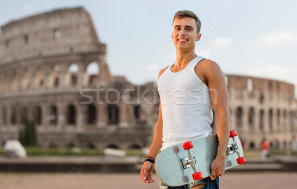 smiling teenage boy with skateboard over coliseum Stock photo © dolgachov