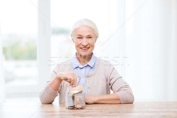 senior woman putting money into glass jar at home Stock photo © dolgachov