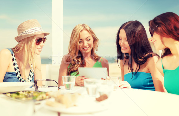 Stock photo: smiling girls looking at tablet pc in cafe