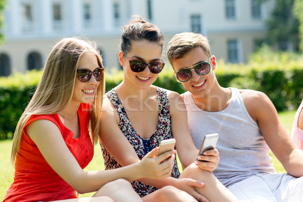 Sorridente amigos smartphones sessão parque amizade Foto stock © dolgachov