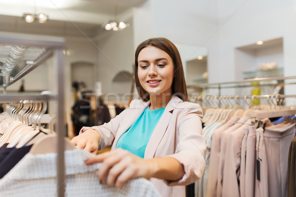 Stock photo: happy young woman choosing clothes in mall