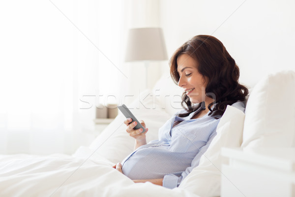 Stock photo: happy pregnant woman with smartphone in home bed