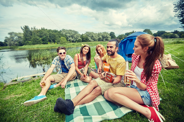 Stock photo: happy friends with drinks and guitar at camping