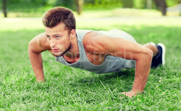 young man doing push ups on grass in summer park Stock photo © dolgachov