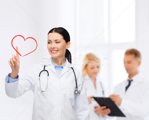 smiling female doctor pointing to heart Stock photo © dolgachov