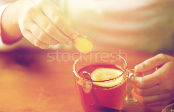 Stock photo: close up of woman adding ginger to tea with lemon