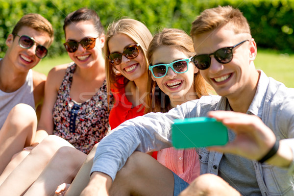 Uśmiechnięty znajomych smartphone posiedzenia trawy przyjaźni Zdjęcia stock © dolgachov