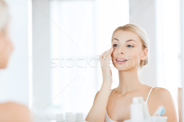 happy woman applying cream to face at bathroom Stock photo © dolgachov