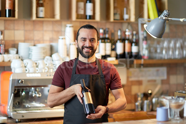 Stock photo: happy man or waiter with bottle of red wine at bar