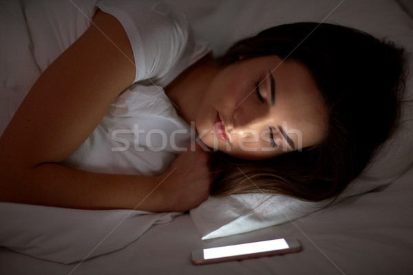 Stock photo: woman with smartphone sleeping in bed at night