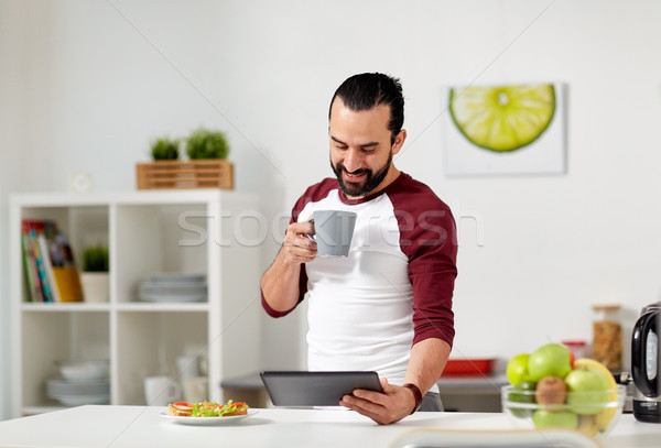 man with tablet pc eating at home kitchen Stock photo © dolgachov