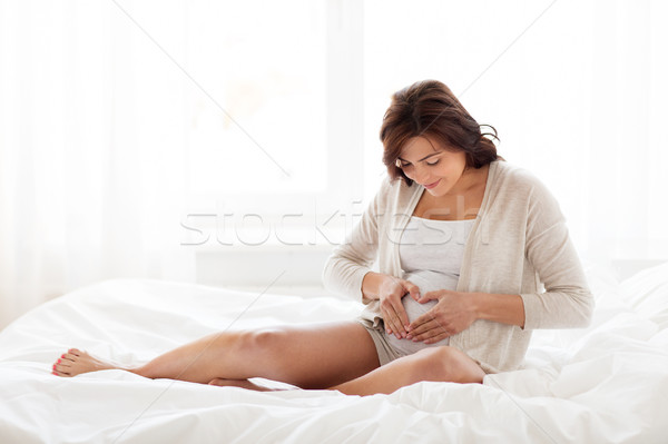 happy pregnant woman making heart gesture at home Stock photo © dolgachov