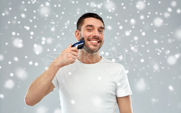 smiling man shaving beard with trimmer over snow Stock photo © dolgachov