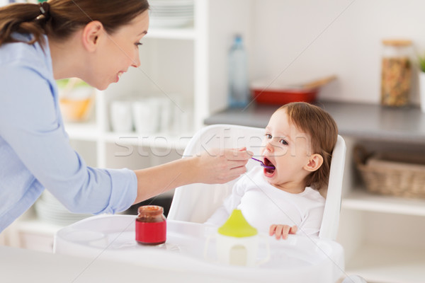 Stock photo: happy mother feeding baby with puree at home