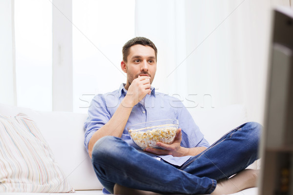 young man watching tv and eating popcorn at home Stock photo © dolgachov