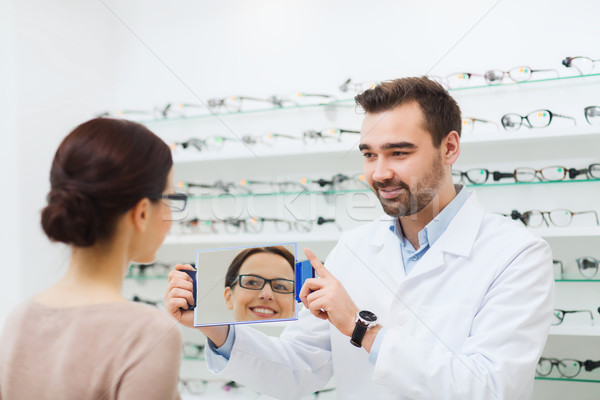 woman in glasses looking to mirror at optics store Stock photo © dolgachov