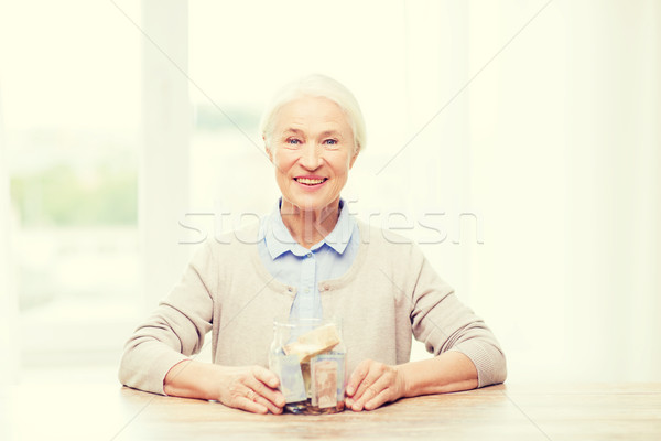 senior woman with money in glass jar at home Stock photo © dolgachov