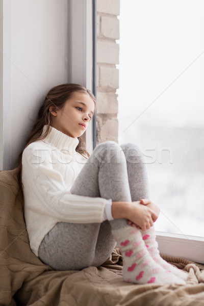 Stock photo: sad girl sitting on sill at home window in winter