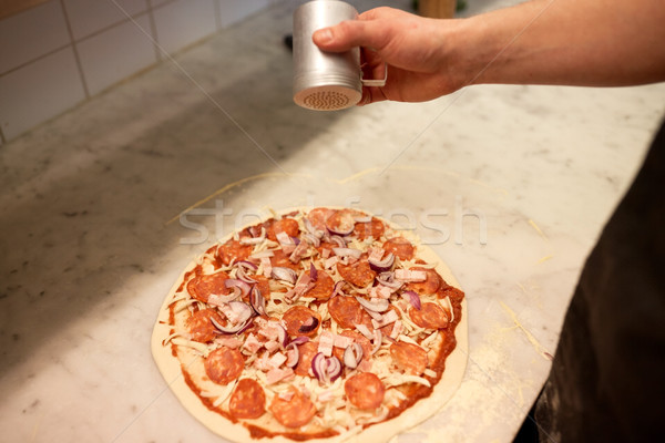 Stock photo: cook adding pepper to salami pizza at pizzeria