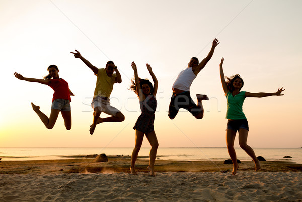 smiling friends dancing and jumping on beach Stock photo © dolgachov
