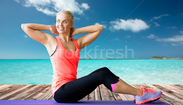 smiling woman doing sit-up on mat over sea Stock photo © dolgachov