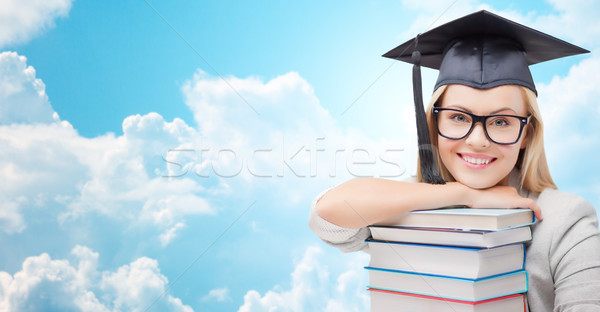 student in trencher cap with books over blue sky Stock photo © dolgachov