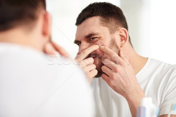 Stock photo: man squeezing pimple at bathroom mirror