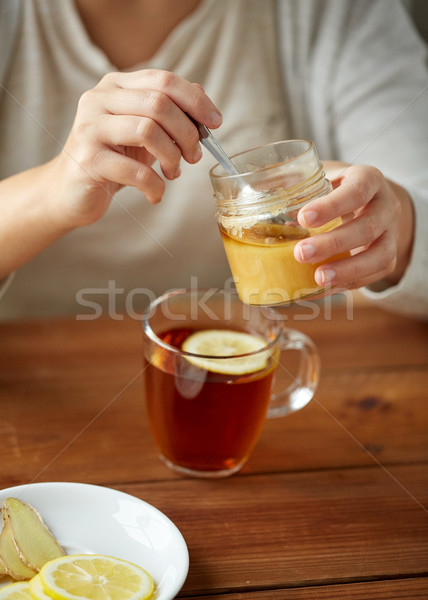 Stock photo: close up of woman adding honey to tea with lemon