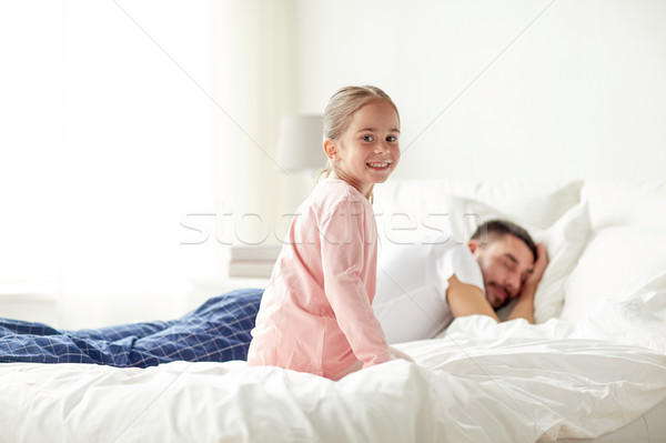 Stock photo: little girl waking her sleeping father up in bed