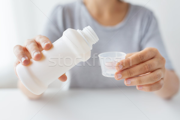 woman pouring syrup from bottle to medicine cup Stock photo © dolgachov