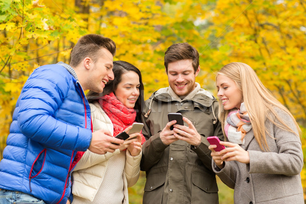 Stock photo: smiling friends with smartphones in city park