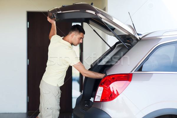 young man with open car trunk at parking space Stock photo © dolgachov