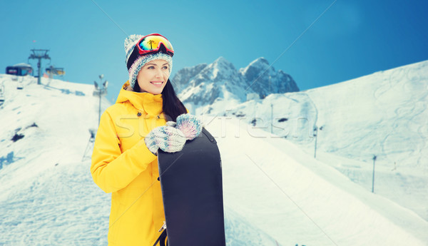 Stock photo: happy young woman with snowboard over mountains