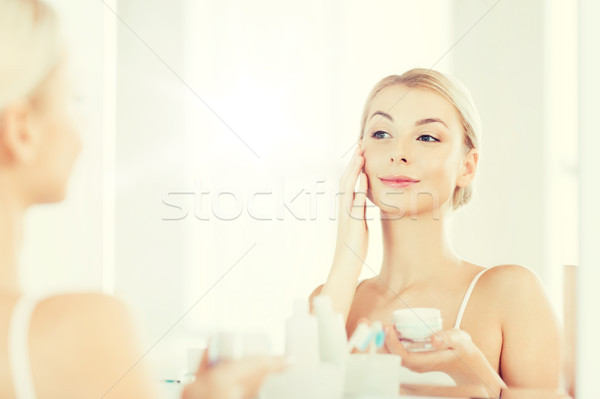 happy woman applying cream to face at bathroom Stock photo © dolgachov