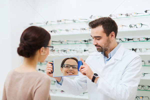 woman in glasses looking to mirror at optics store Stock photo © dolgachov