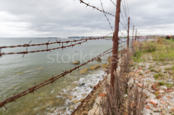 Stock photo: barb wire fence over gray sky and sea