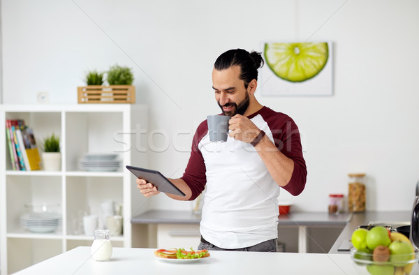 man with tablet pc eating at home kitchen Stock photo © dolgachov