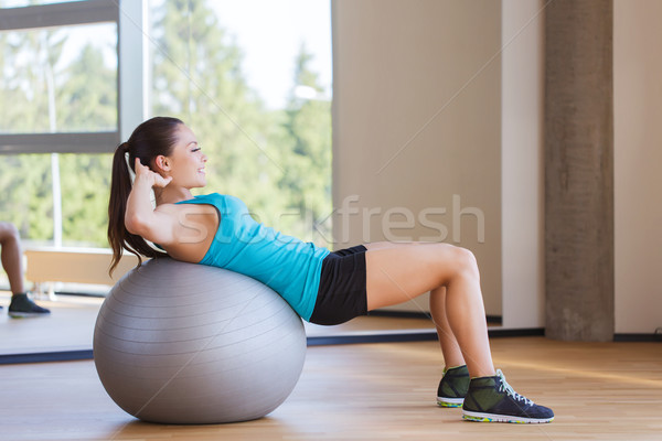 Stock photo: smiling woman with fit ball flexing muscles in gym