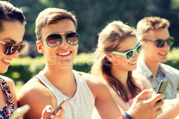 Stock photo: smiling friends with smartphones sitting in park