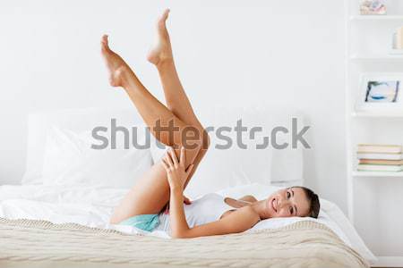 happy young woman with pillow lying in bed at home Stock photo © dolgachov
