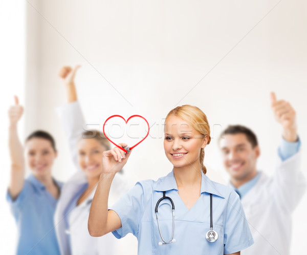 smiling doctor or nurse drawing red heart Stock photo © dolgachov