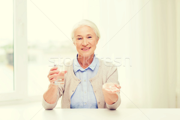 happy senior woman with water and medicine at home Stock photo © dolgachov