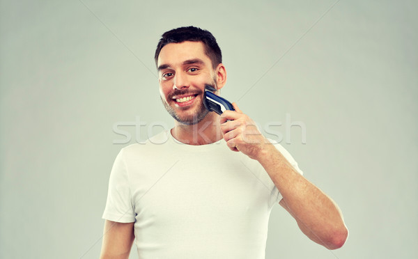 smiling man shaving beard with trimmer over gray Stock photo © dolgachov