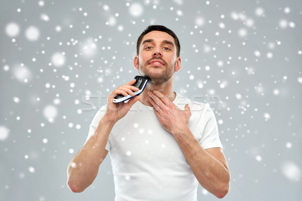 smiling man shaving beard with trimmer over snow Stock photo © dolgachov