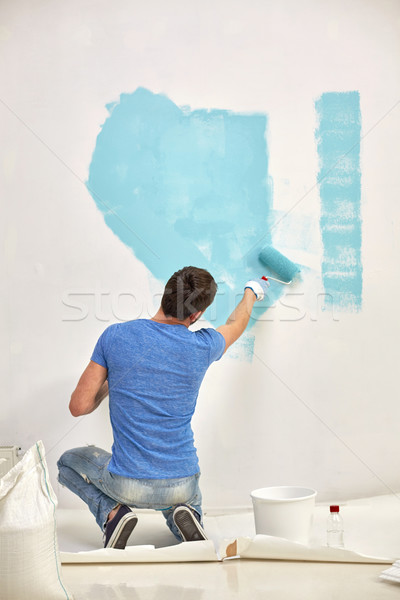 Stock photo: man with roller painting wall in blue at home